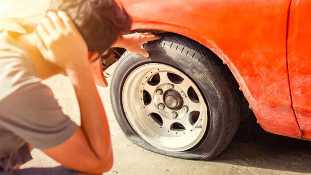 homem com a mão na nuca, olhando para pneu furado do carro laranja