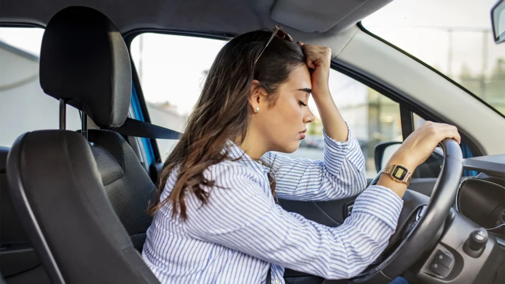 mulher dentro do carro com olhos fechados e mão na cabeça