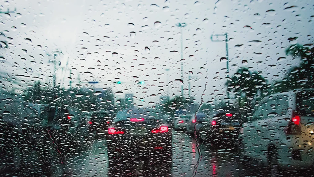 vidro com gotículas de agua na chuva, com carro a frente