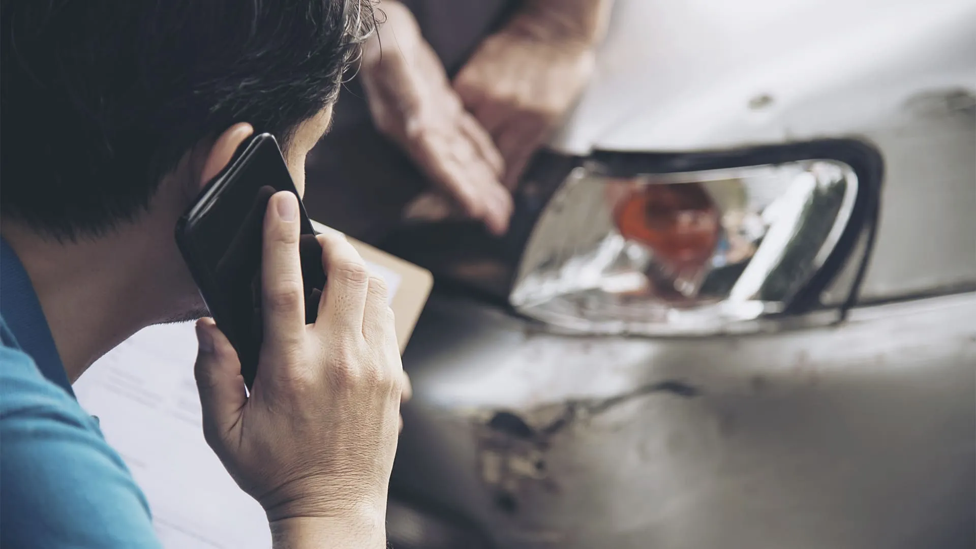 Perda Total homem falando ao celular olhando para um carro batido.