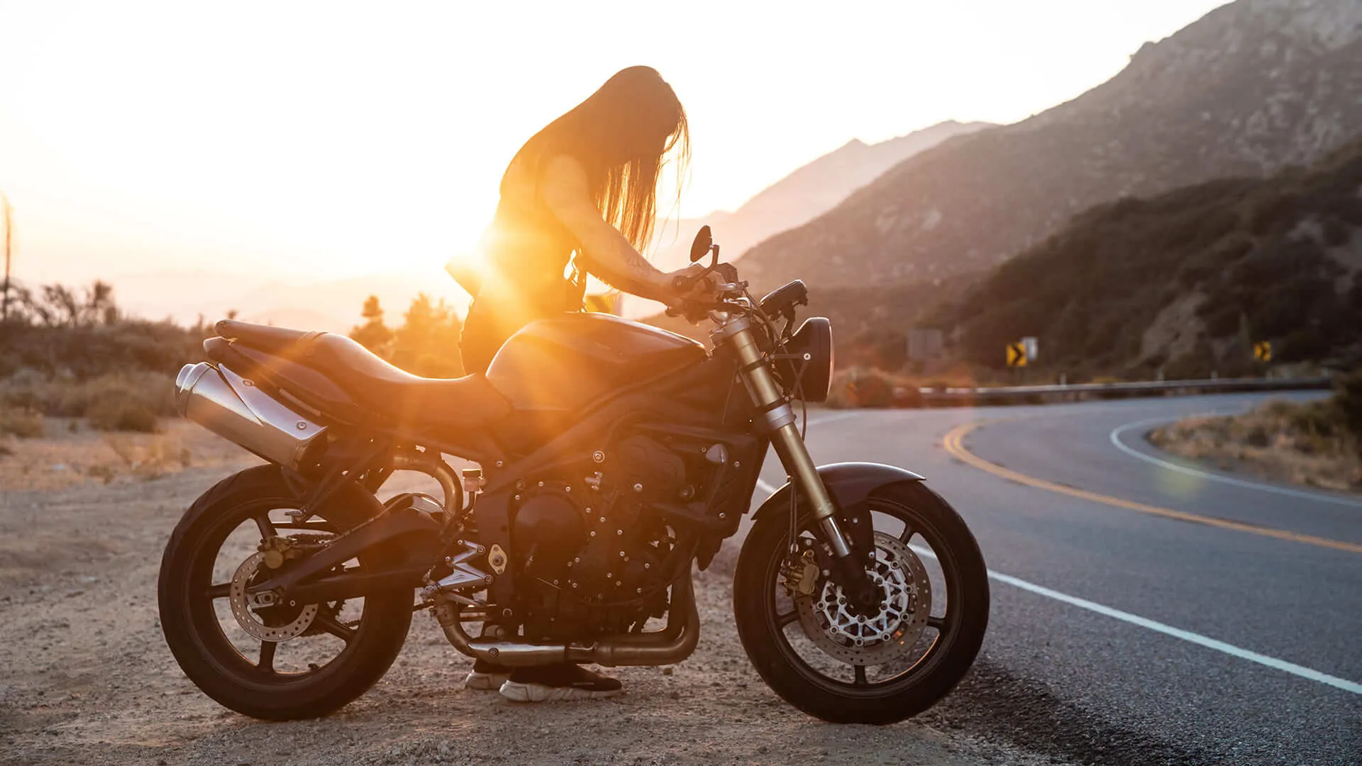proteção veicular Mulher ao lado da sua moto olhando para o por do sol.