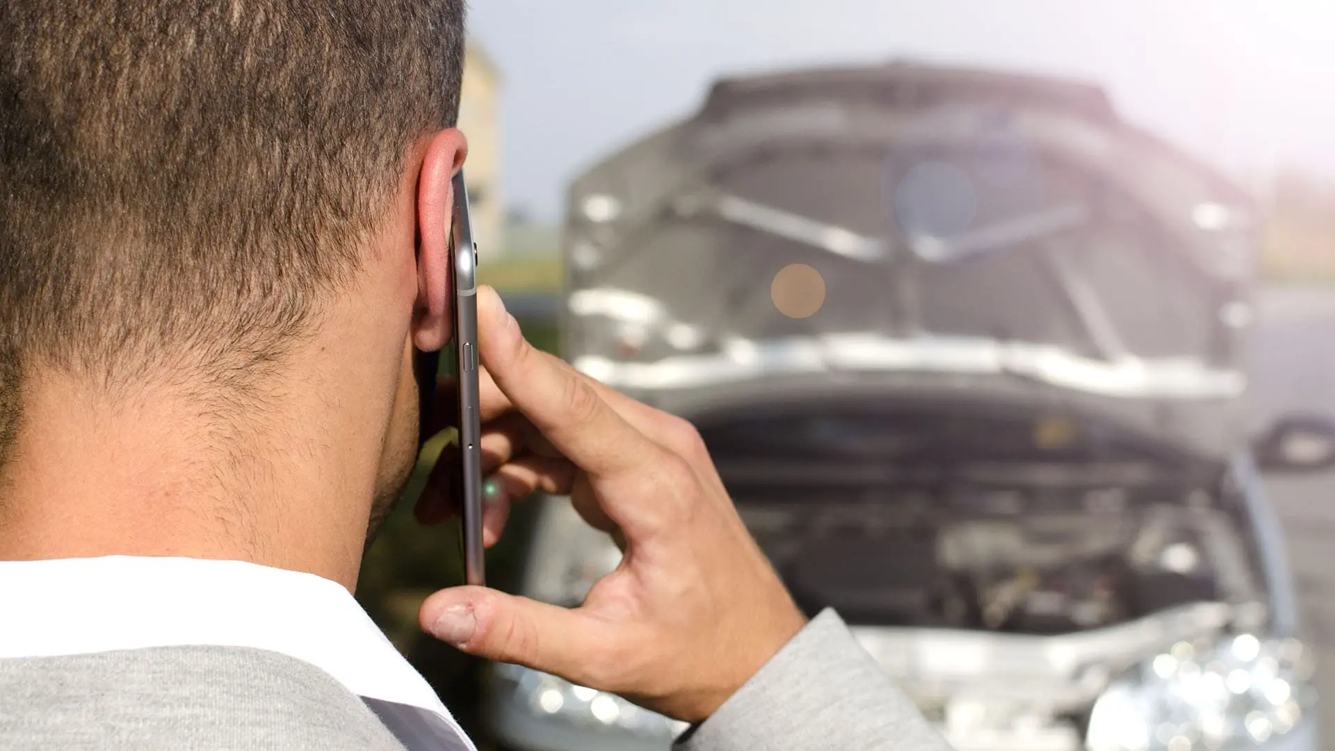homem falando no celular olhando para carro com capo aberto. proteção veicular